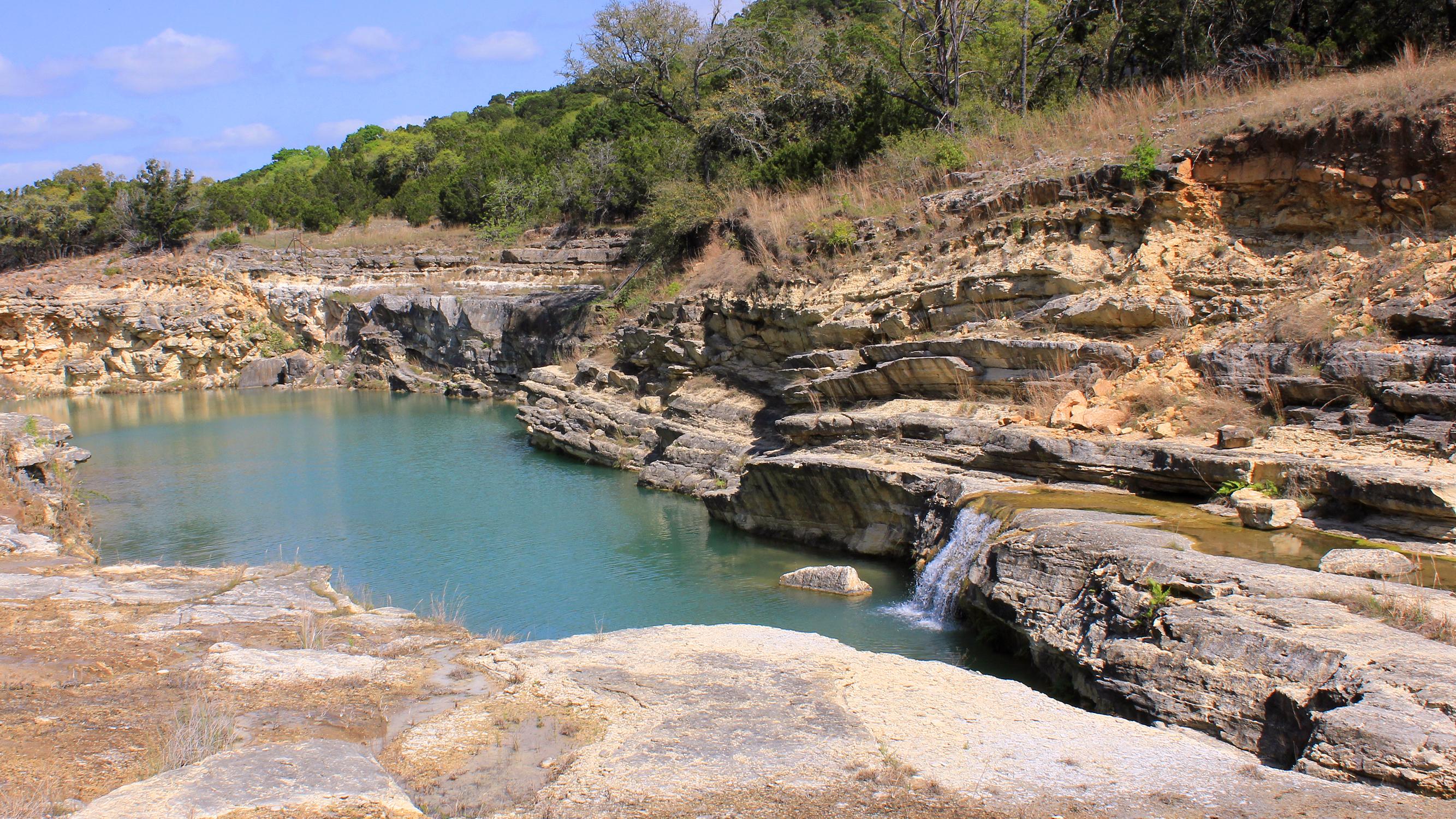 A turquoise plunge pool below a small limestone waterfall in a layered rock gorge