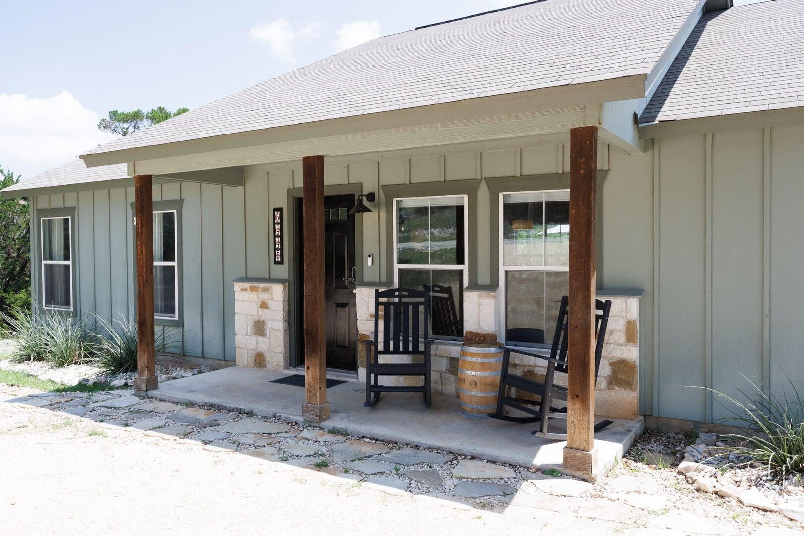 Covered front porch with cedar posts, rocking chairs, and a whiskey-barrel table