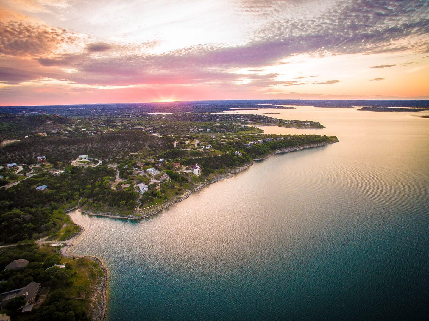 Aerial view of Canyon Lake at sunset, a wooded shoreline curving into calm water under a pink sky