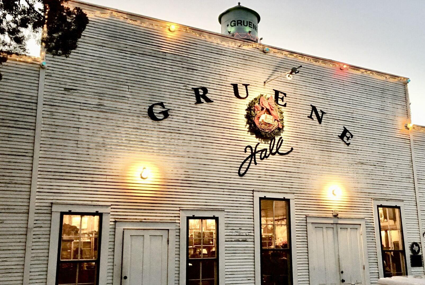 The white clapboard exterior of Gruene Hall at dusk with the Gruene water tower rising behind it