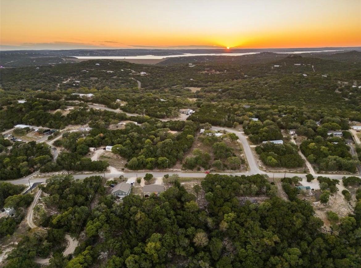 Aerial view of a wooded Hill Country neighborhood at sunset with Canyon Lake on the horizon